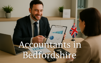 A professional accountant in a modern Bedfordshire office explains financial charts to a client across a tidy desk with a laptop, spreadsheets, and calculators. A small British flag and HMRC document in the background suggest a UK business setting. Overlay text reads Accountants in Bedfordshire