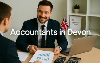 A professional accountant in a modern Devon office explains financial charts to a client across a tidy desk with a laptop, spreadsheets, and calculators. A small British flag and HMRC document in the background suggest a UK business setting. Overlay text reads Accountants in Devon