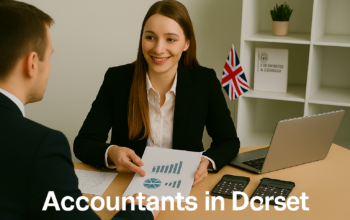 A professional accountant in a modern Dorset office explains financial charts to a client across a tidy desk with a laptop, spreadsheets, and calculators. A small British flag and HMRC document in the background suggest a UK business setting. Overlay text reads Accountants in Dorset
