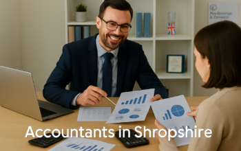 A professional accountant in a modern Shropshire office explains financial charts to a client across a tidy desk with a laptop, spreadsheets, and calculators. A small British flag and HMRC document in the background suggest a UK business setting. Overlay text reads Accountants in Shropshire