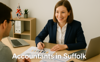 A professional accountant in a modern Suffolk office explains financial charts to a client across a tidy desk with a laptop, spreadsheets, and calculators. A small British flag and HMRC document in the background suggest a UK business setting. Overlay text reads Accountants in Suffolk