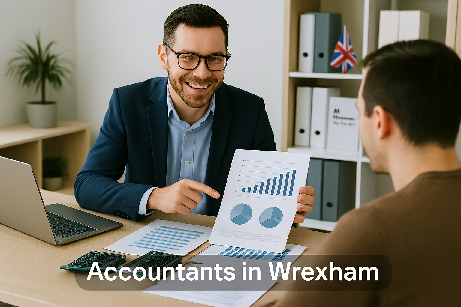 A professional accountant in a modern Wrexham office explains financial charts to a client across a tidy desk with a laptop, spreadsheets, and calculators. A small British flag and HMRC document in the background suggest a UK business setting. Overlay text reads Accountants in Wrexham